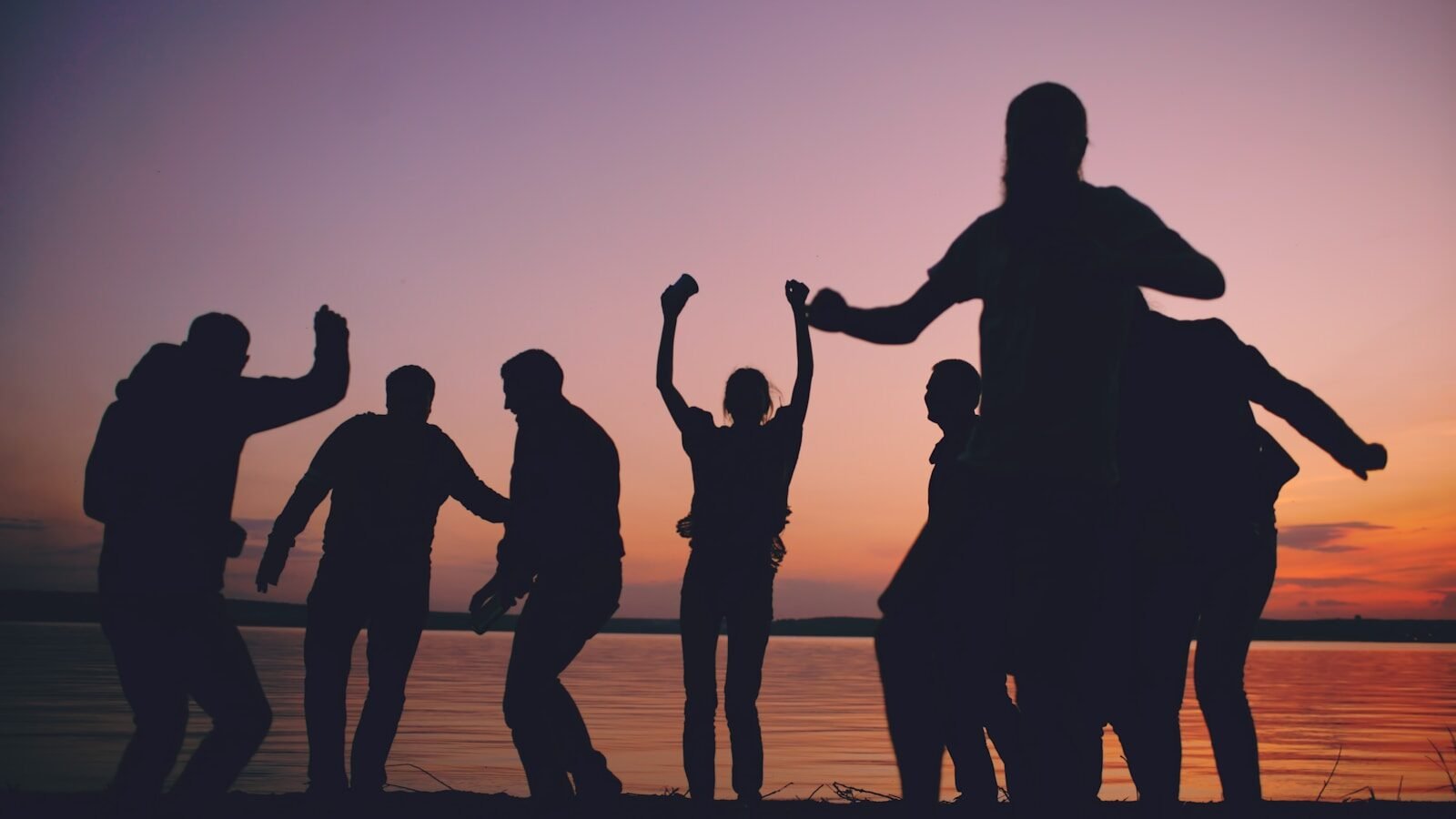 Silhouettes of friends celebrating at sunset by the water